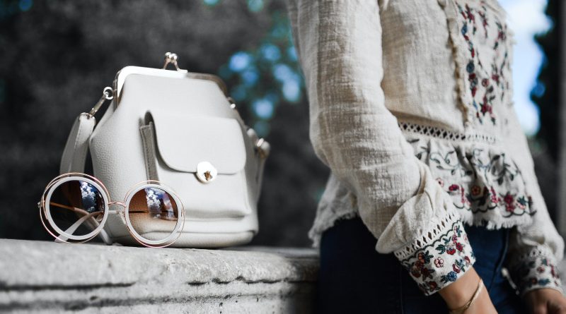 woman wearing beige and red floral top leaning on gray concrete slab with white leather bag ontop